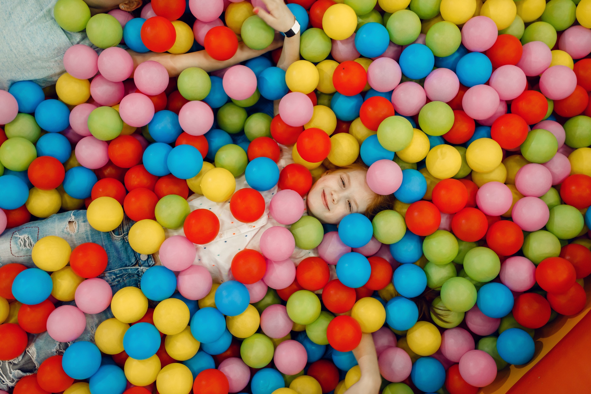 Girl lying among many colorful balls, playground