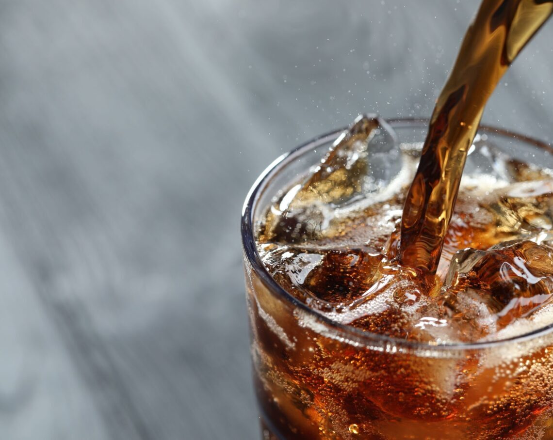 Pouring refreshing cola into glass on blurred grey background, closeup. Space for text